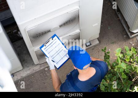 Two Electricians Men Wearing Safety Jackets Checking Air Conditioning Unit On Building Rooftop Stock Photo