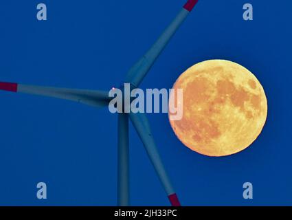 Sieversdorf, Germany. 12th July, 2022. The moon, which is about 95 percent visible and waxing, glows yellowish in the sky next to a wind turbine shortly after sunset. On the night of July 13, 2022, a super full moon can be seen in the sky with good visibility. At moonrise around 10 p.m., the Earth's satellite will be 357,517 kilometers from Earth. Despite this distance, it will be the largest supermoon of the year. Credit: Patrick Pleul/dpa/Ģ����ý Live News Stock Photo