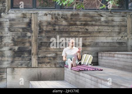 Software developer wearing glasses using laptop and phone, distracted by his gadget during working Stock Photo