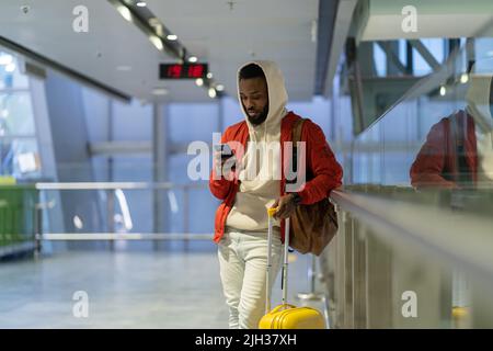 Young African man traveler with baggage surfing internet or connecting to free airport wifi Stock Photo