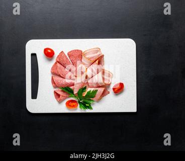 Food meat assortment bacon sausage salami slices on a cutting white board on a black background, Stock Photo