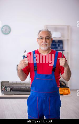Old male repairman repairing air-conditioner Stock Photo