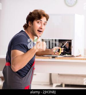 Young handsome contractor repairing fridge Stock Photo