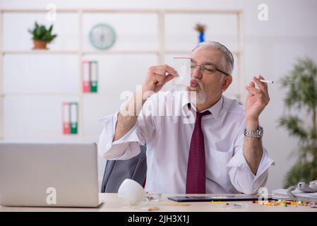 Old male drug addicted employee sitting at workplace Stock Photo