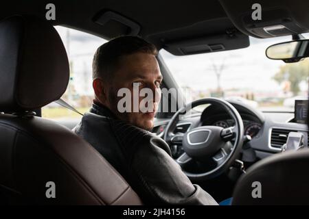 A man looks from behind the wheel of the car to the back of the car in astonishment. Front view. Stock Photo