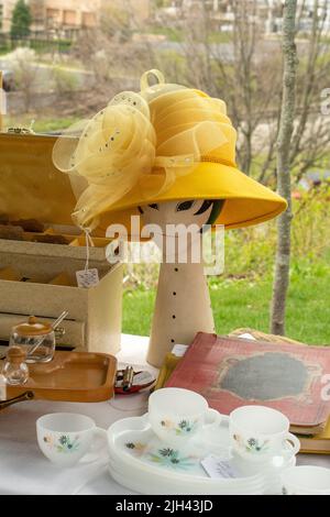 A mannequin wears a fancy yellow hat at a tag sale, with tea items and other fun items on display for purchase Stock Photo