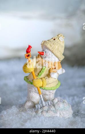 Comical snowman with a snow shovel, engages with a tiny red cardinal who lands on the shovel handle Stock Photo