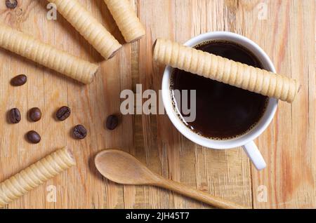 Chocolate wafer rolls and cup of coffee on old wooden background, top view Stock Photo