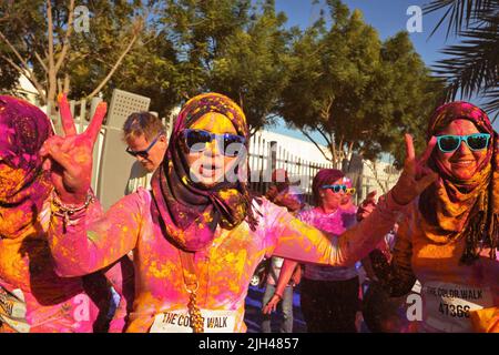 Covered in colored powder, animated Arab woman with Hijab and blue shades holds up two peace signs at the Color Walk in Dubai, United Arab Emirates. Stock Photo