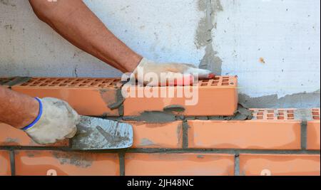 Close up on bricklaer hands laying house brick wall with  trowel. Stock Photo