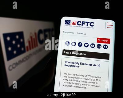 Person holding cellphone with webpage of US Commodity Futures Trading Commission (CFTC) on screen with logo. Focus on center of phone display. Stock Photo
