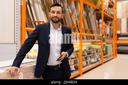 a man in a business suit next to a showcase of building materials in a hypermarket Stock Photo