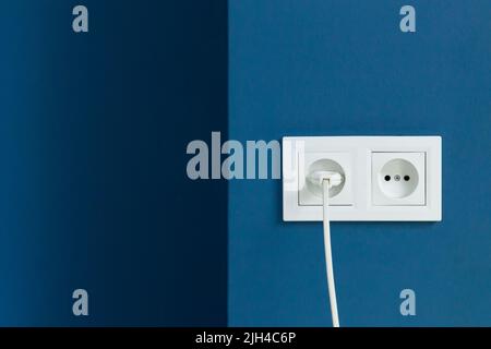 White electrical plug in the electric double socket on a blue wall Stock Photo