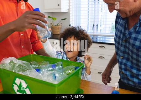 Multiracial father and grandfather teaching boy to recycle waste by throwing plastic bottles in bin Stock Photo