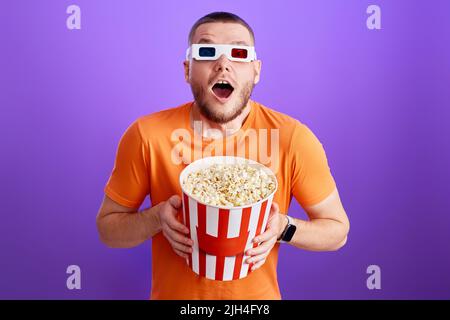 Young caucasian man in 3d glasses eating popcorn Stock Photo
