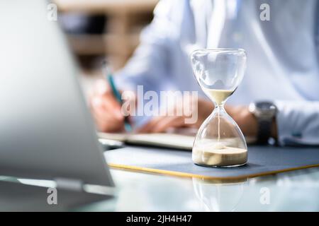 Close-up Of Hourglass In Front Of Businessperson's Hand Calculating Invoice Stock Photo