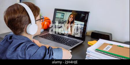 Boy with headphones receiving class at home with laptop from his Stock Photo