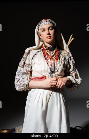 young ukrainian woman in traditional clothing with ornament holding wheat spikelets on black Stock Photo
