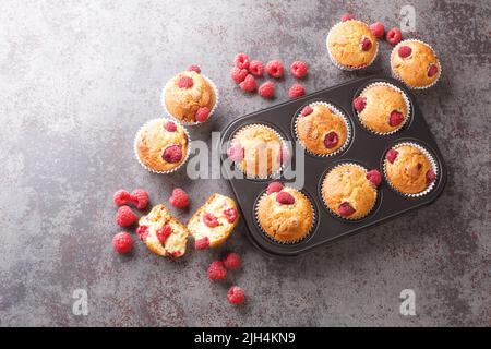 Freshly baked muffins with raspberries and white chocolate close-up in a muffin pan on the table. Horizontal top view from above Stock Photo