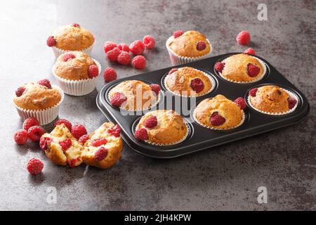 Freshly baked muffins with raspberries and white chocolate close-up in a muffin pan on the table. Horizontal Stock Photo