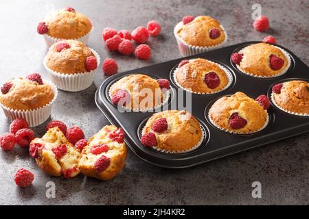 Baked raspberry muffins with white chocolate and fresh berries close-up in a muffin pan on the table. Horizontal Stock Photo