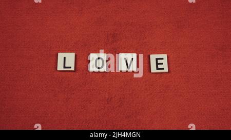 Word "Love" composed of wooden tiles with letters on a red background Stock Photo