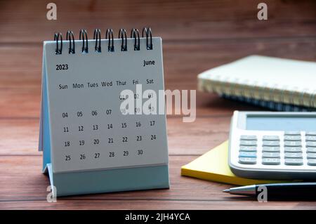 June 2023 white desk calendar on wooden table with notepad, calculator and pen background. New year concept and copy space