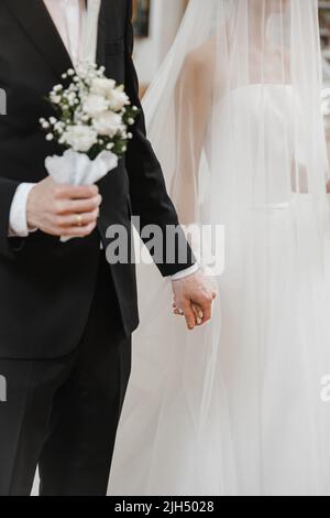 Close up of the groom hand holding the bride wrist. Wedding couple. Newlyweds holding hands in the church Stock Photo