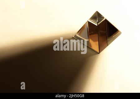 Minimalist still life image of a shiny pyramid in warm color tone. Pyramid throwing hard shadow. Stock Photo