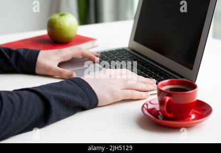 Man hands on laptop keyboard with notebook, green apple and red cup of coffee on white table Stock Photo