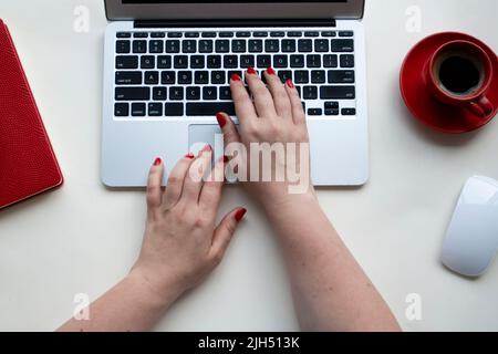 Woman hands on laptop keyboard with wireless mouse, cup of coffee, notebook on white table Stock Photo
