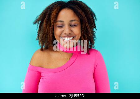 Dreamy young beautiful African American woman with bright eyelines wearing pink bodysuit over blue wall keeps her eyes closed, looks with happy expres Stock Photo