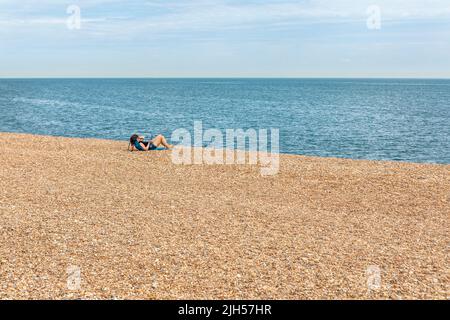 A young woman alone on a shingle beach reading Stock Photo