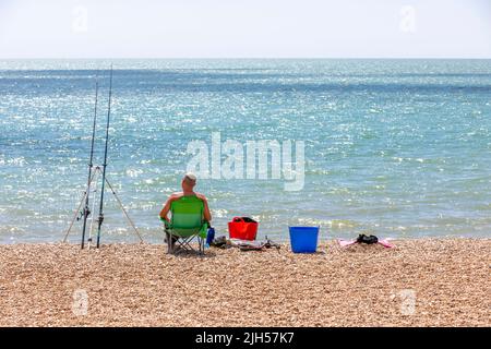 A fisherman sat in a chair on a shingle beach Stock Photo