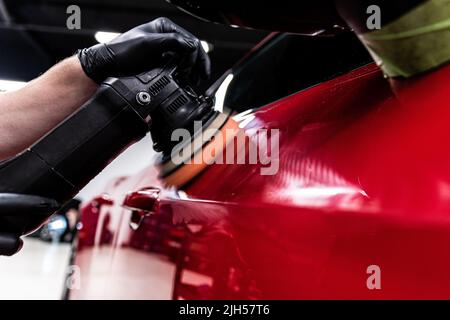 Employee of a car wash or a car detailing studio polishes the car paint Stock Photo