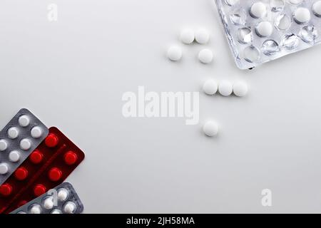 On a white background on the left are three blisters with pills, on the top right are round white loose pills and packaging from them Stock Photo