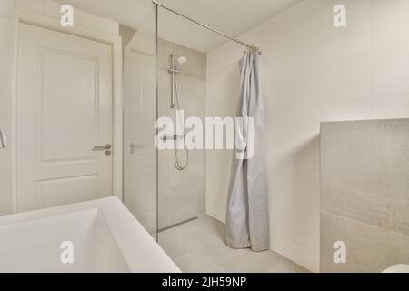 Bathtub located near shower box with glass door in modern bathroom with white tiled walls Stock Photo