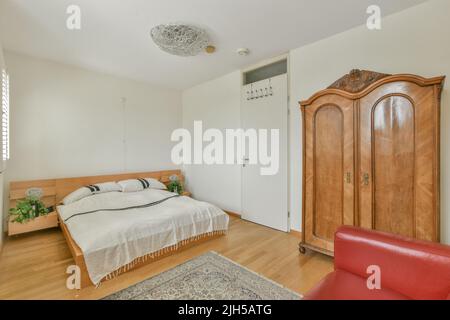 Comfortable bed with ornamental blanket placed near glass door and wardrobe with mirror in light bedroom Stock Photo