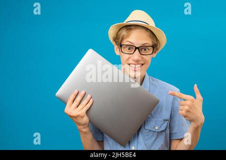 Waist up portrait view of the funny teen person holding laptop in hands. Indoor studio shot isolated on blue background Stock Photo
