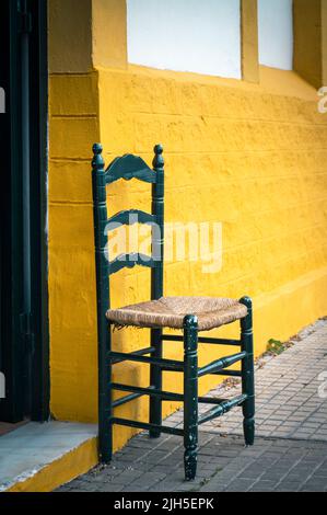 A chair outside an old sherry warehouse and bodega painted yellow, by Gutierrrez Colosia in Puerto de Santa Maria Spain Stock Photo