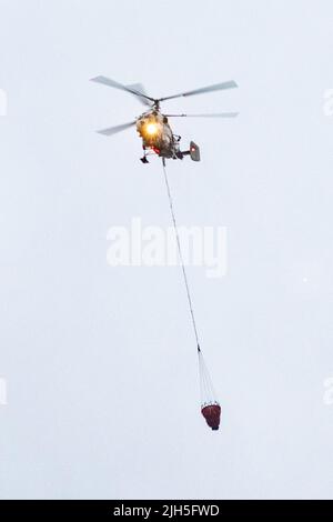 A fire helicopter carries a container of water to extinguish a fire in a production building Stock Photo