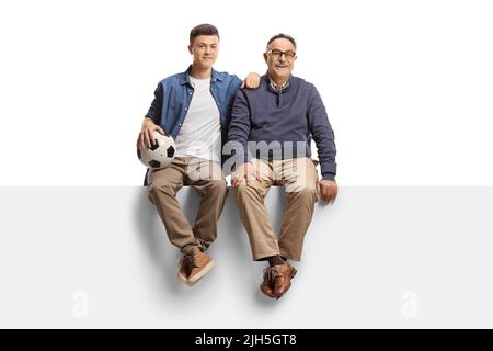 Guy and a mature man sitting on a panel and holding a soccer ball isolated on white background Stock Photo