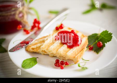 fried bread croutons for breakfast with redcurrant jam in a plate with berries on a wooden table. Stock Photo