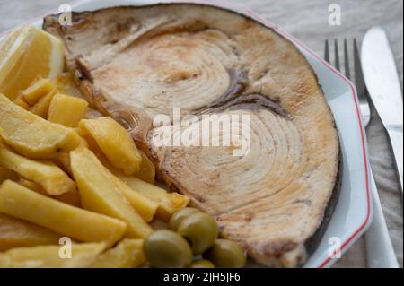 Seafood dish, grilled steak from swordfish or spada served with french fried potatoes and green olives, close up Stock Photo