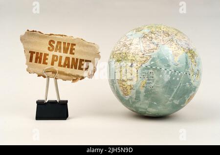 Ecological concept. Near the globe there is a clip with a cardboard plate on which it is written - Save The Planet Stock Photo