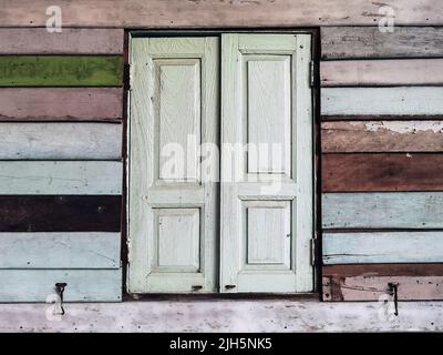 Old grunged wooden window frame painted white vintage with old colourful plywood wall. Antique window frame and old panes. Old closed window and plank Stock Photo