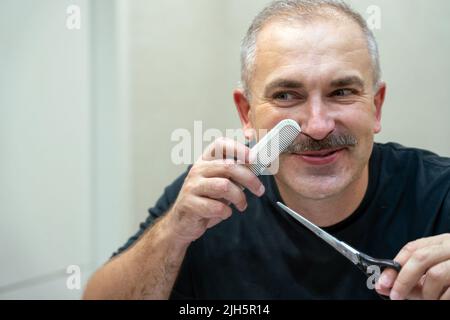 Middle-aged handsome man using scissors to cut his mustache Stock Photo