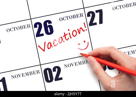 26th day of October. A hand writing a VACATION text and drawing a smiling face on a calendar date 26 October. Vacation planning concept. Autumn month, Stock Photo