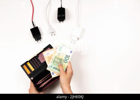 Woman hand takes Euro money banknotes from wallet near many power cable cords with Eu plugs on white background. Electricity cost and expensive energy Stock Photo