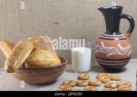 White bread with sunflower seeds and sesame baguette and bun in a ceramic dish. Bagels, a glass of milk and a ceramic jug Stock Photo